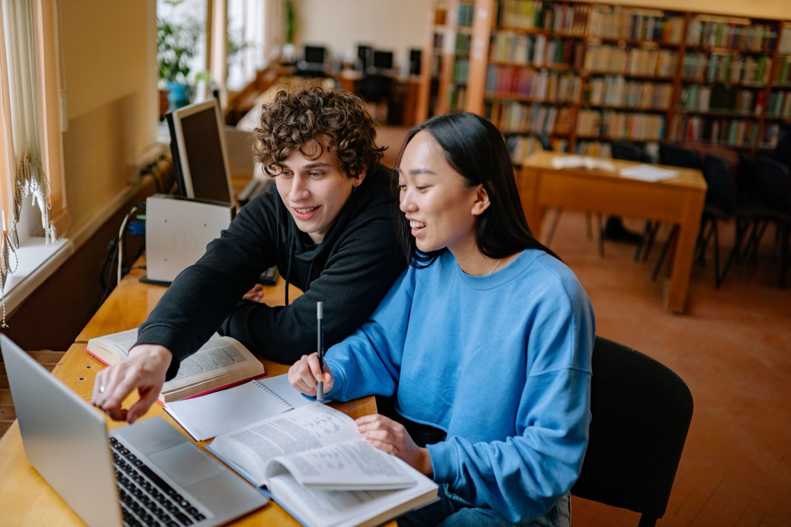 Two students studying together with a laptop and textbooks in a library