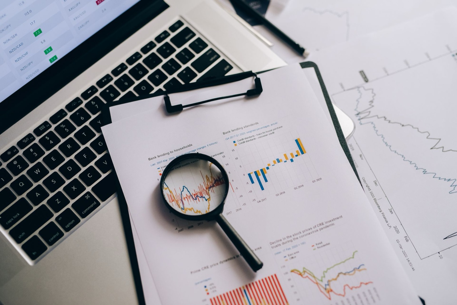 A magnifying glass resting on printed charts beside a laptop