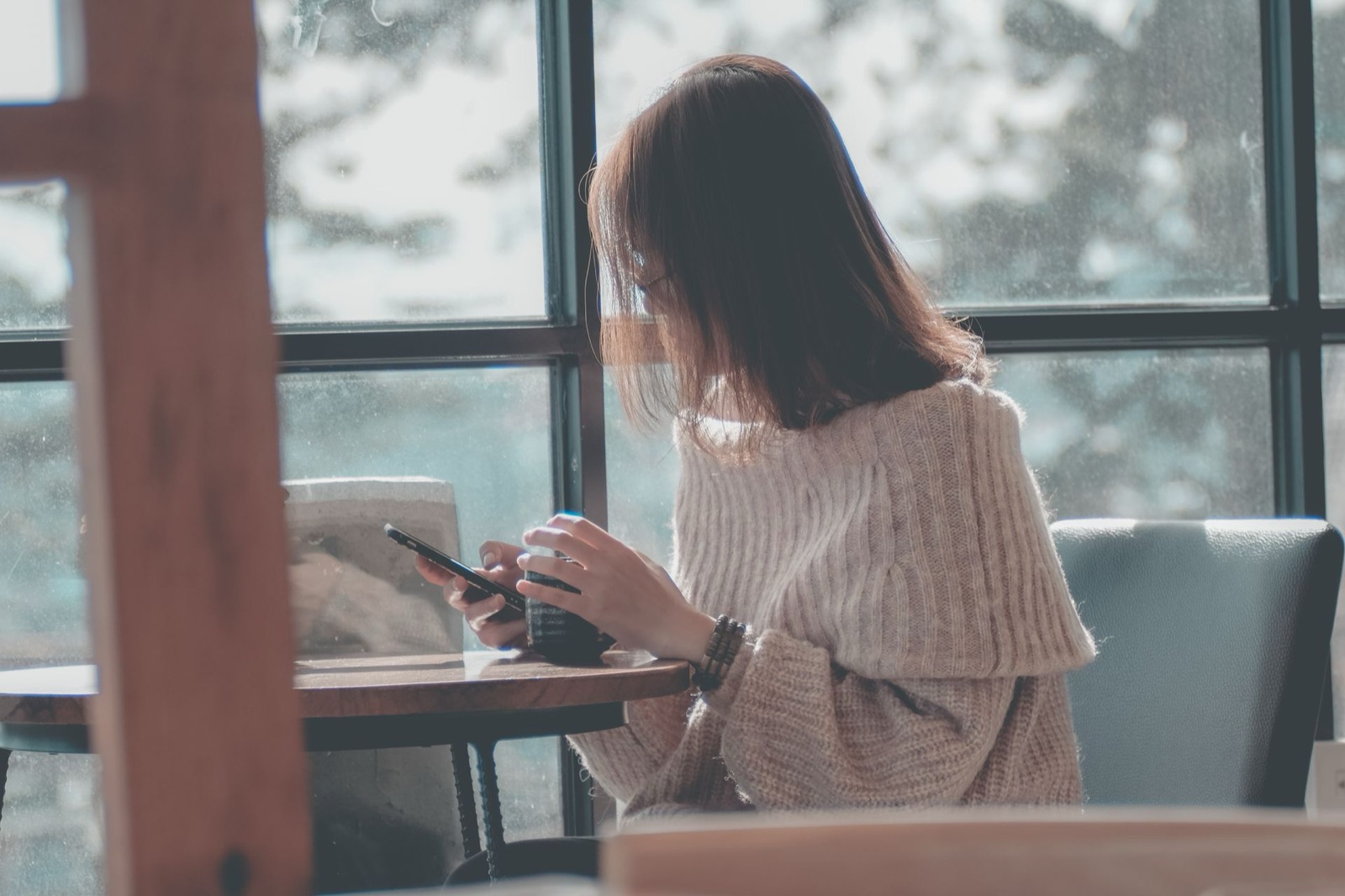 A woman checking her smartphone at a cafe table by a window